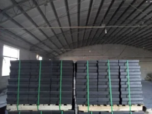 Two pallets of dark magnesia-carbon bricks secured with green strapping inside a steel-roofed warehouse